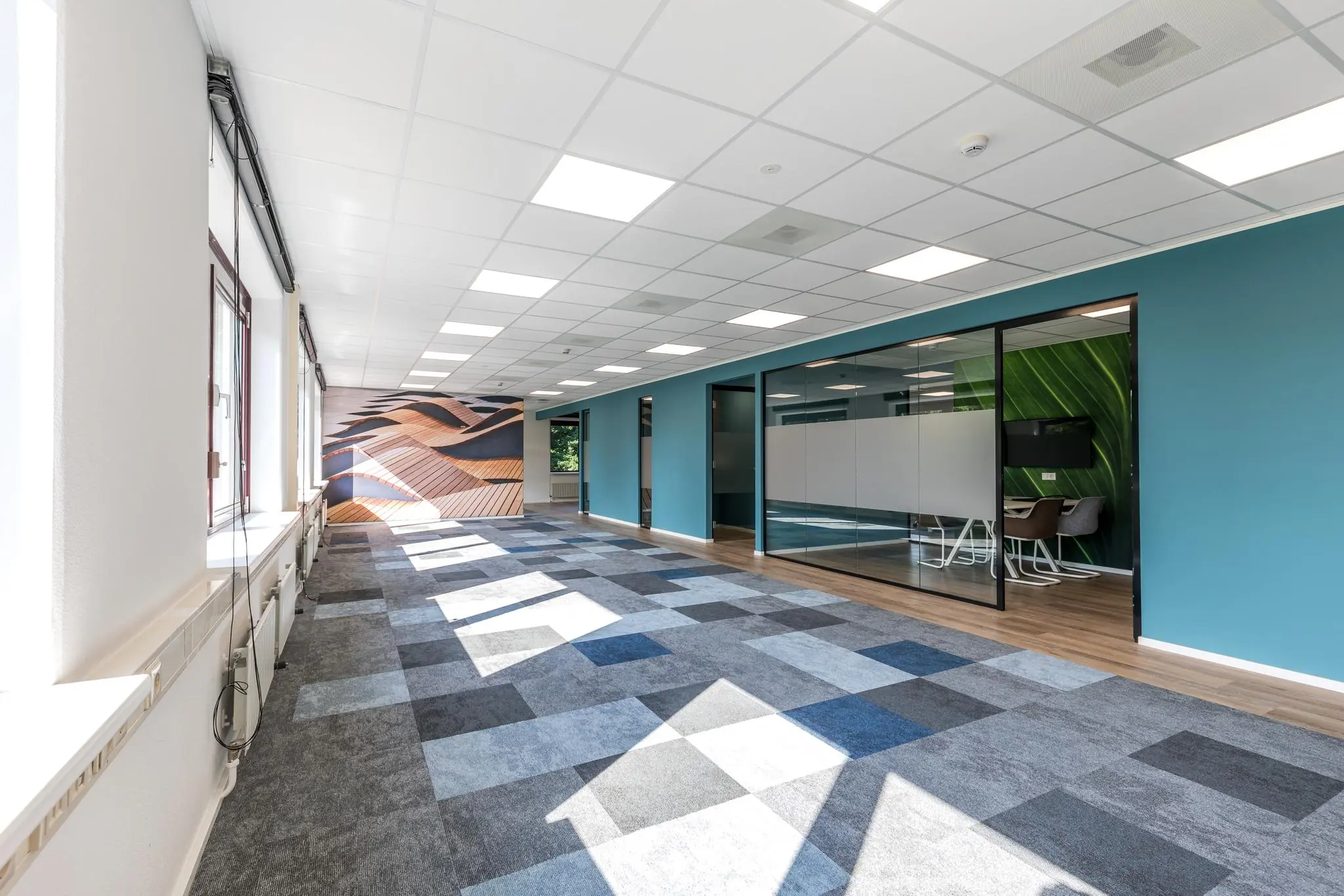 Licht en modern kantoorinterieur aan de Baarnsche Dijk met glazen vergaderruimte en kleurrijk tapijt.